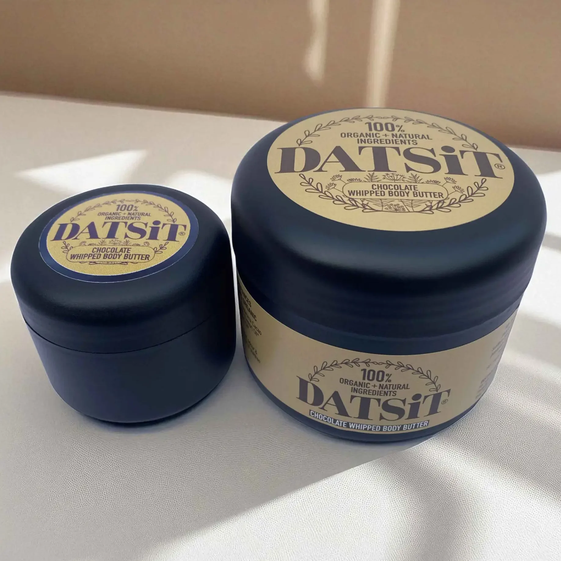 Two jars of Datsit organic chocolate whipped body butter, one 50ml jar, and one 150ml jar on a muted background with soft shadows